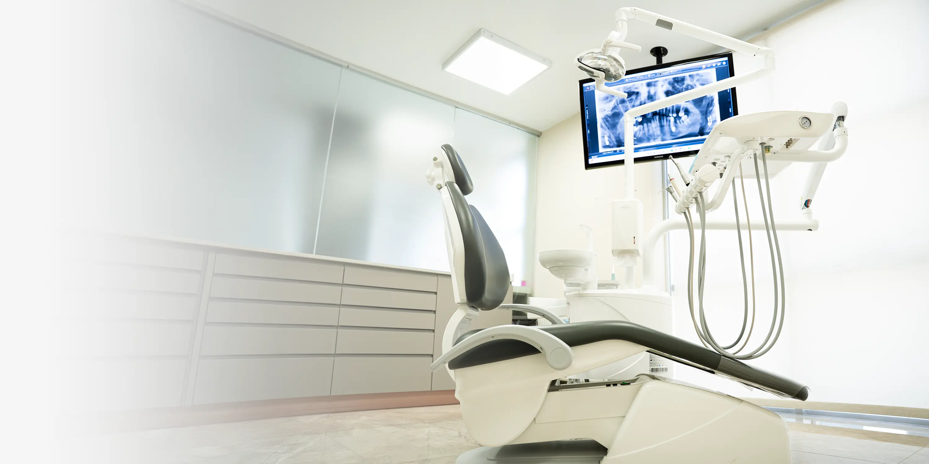 DentVisit treatment room with a dental chair, overhead light and a chairside screen showing a panoramic dental X-ray